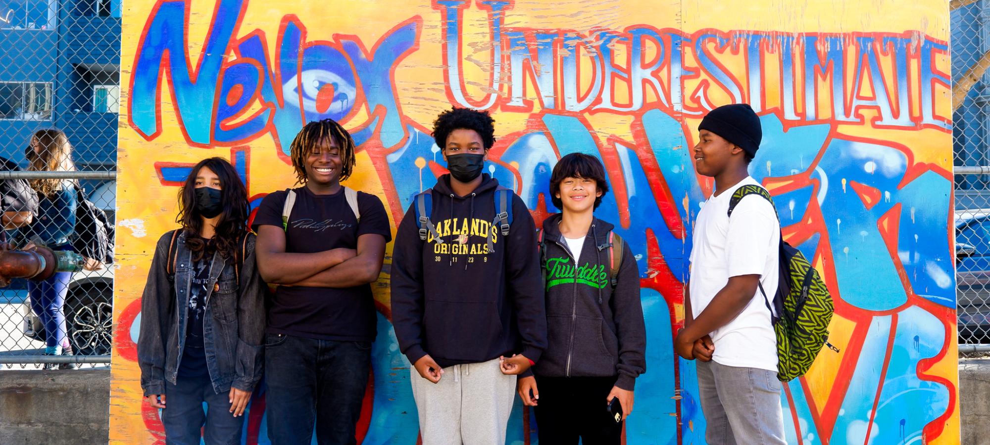 Students pose in front of a mural